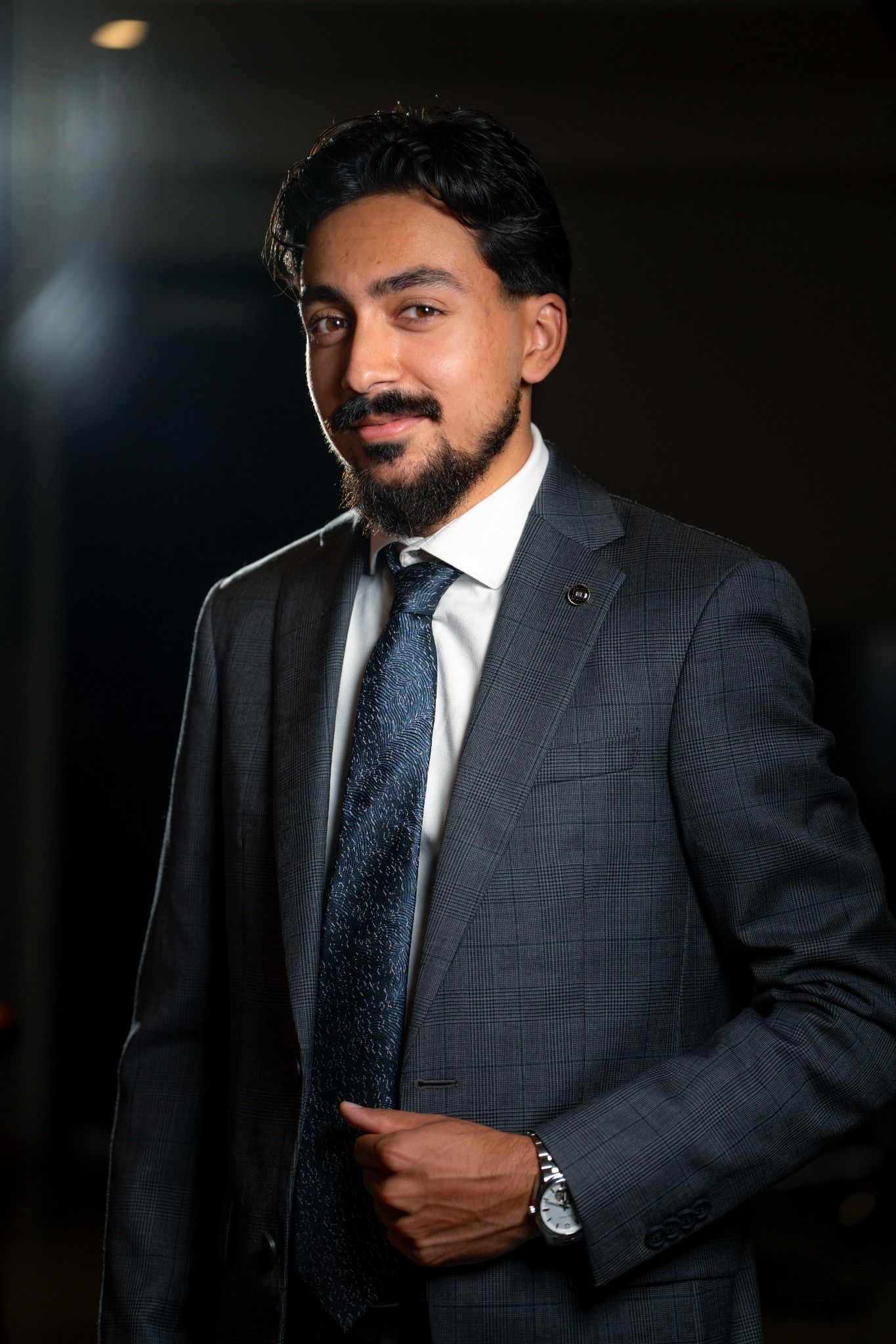 Siraaj Shah standing in a grey suit, smiling toward the camera